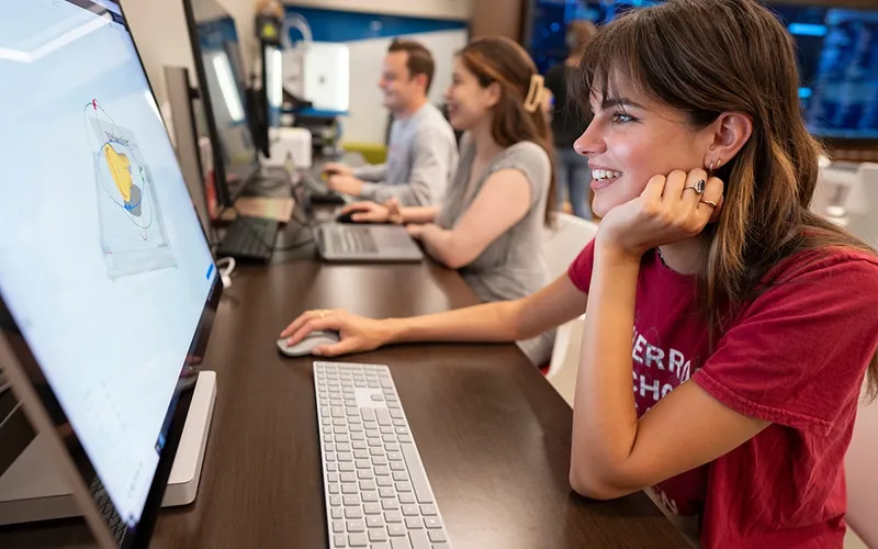 Students sitting at a classroom table using computers.
